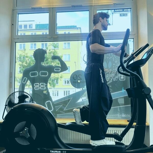 Kardio mit EMS: Mann trainiert auf dem Crosstrainer im EMS-Anzug Kardio mit EMS: Mann trainiert auf dem Crosstrainer im EMS-Anzug